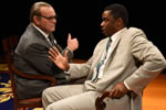 Johnson in charcoal suit and wearing glasses sits next to but opposite King in light tan suit and blue and tan tie, his right hand gesturing.