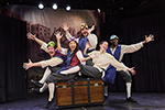 The "Capulet Cast" sitting on or pushing a trunk, in costume, masks pulled up on the top of their heads, and arms spread in greeting. 